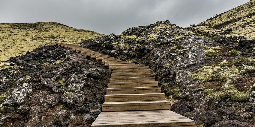 Ancient stone steps leading to a temple surrounded by green hills and a clear blue sky