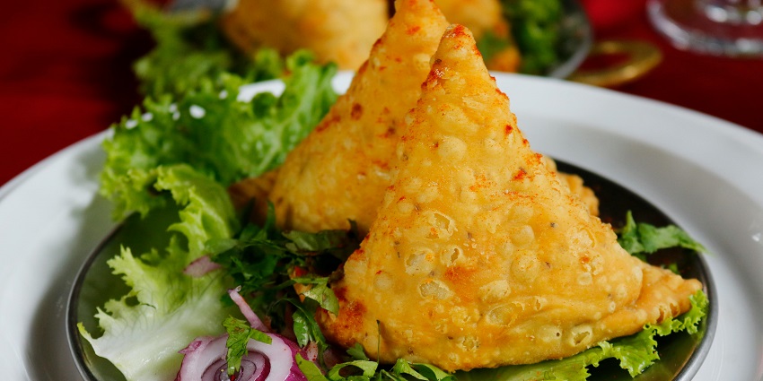 Two pieces of Samosa served on lettuce leaves on a plate alongside fresh onion slices