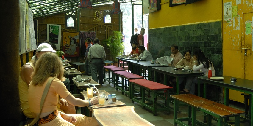 People sitting on benches with tables in the German Bakery decorated with colourful artworks.