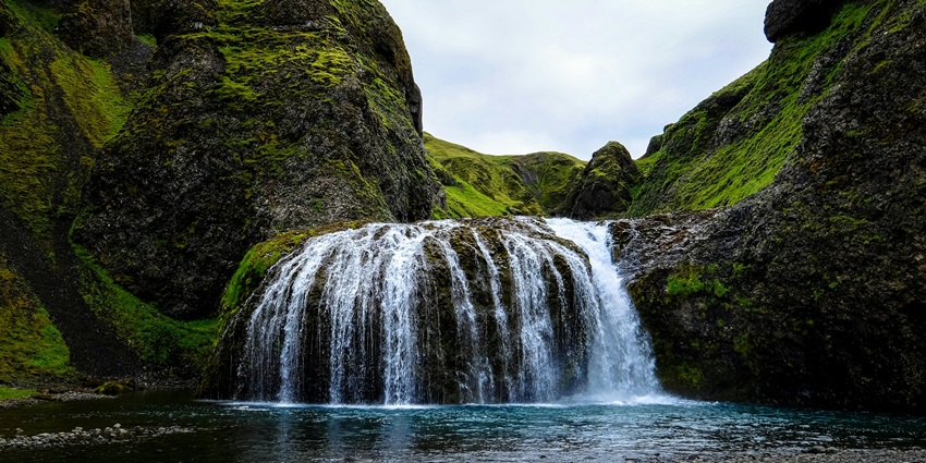 An image of the Gitgit Waterfall cascading down amidst a tropical forest, surrounded by greenery
