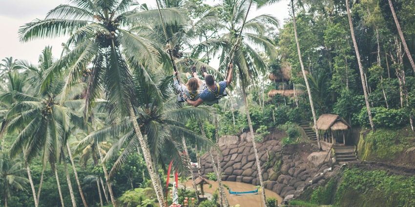Image of a couple swinging in the jungle with a serene view of Bali island, Indonesia