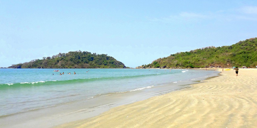 A picture of a beach in Goa, surrounded by the most pretty lush green mountains.