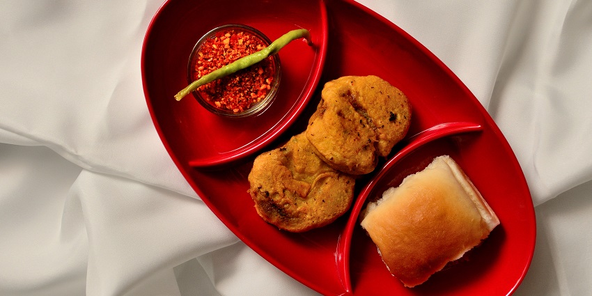 A deep-fried potato patty with bread, fried chilli, and chutney, constituents of Vada Pav