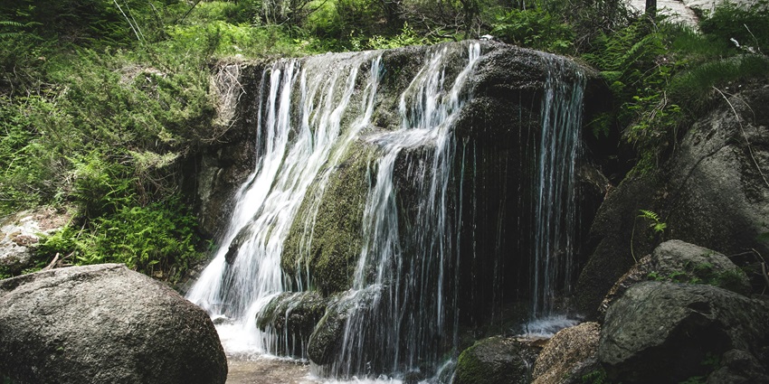 Cascading waterfalls flow over a rocky formation in a dense green landscape