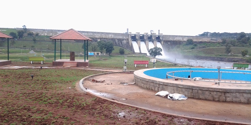 Harangi Dam with a scenic reservoir and surrounding green hills under a clear sky.