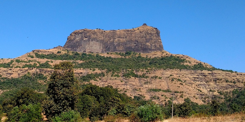 A glimpse of the rustic Harihar Fort perched atop a hill and surrounded by greenery.