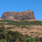 The steep rocky cliffs of Harihar Fort rise, showcasing the fort's structure.