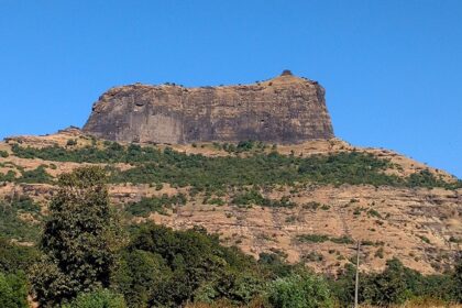 The steep rocky cliffs of Harihar Fort rise, showcasing the fort's structure.