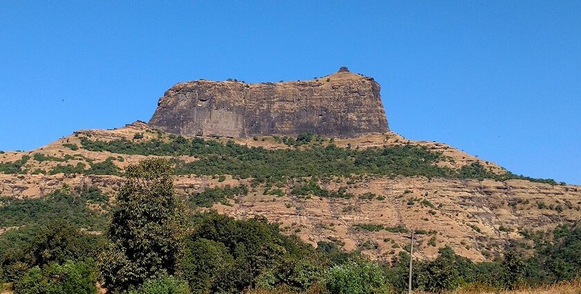 The steep rocky cliffs of Harihar Fort rise, showcasing the fort's structure.