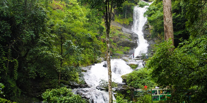 A picture of a beautiful waterfall cascading down a lush green mountain near Kabini