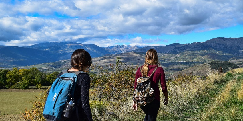 Two women walking towards an open field, enjoying a peaceful outdoor stroll under a cloudy sky