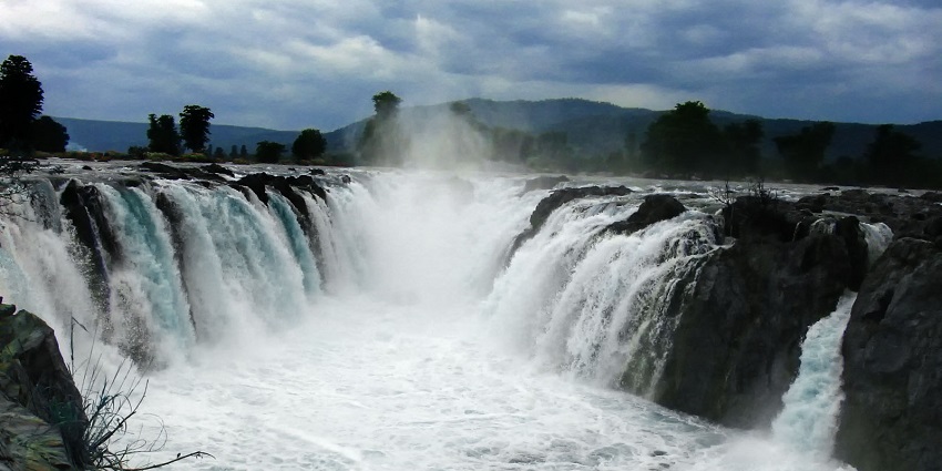 Hogenakkal Falls over dark rocks, creating mist and white water under a cloudy sky