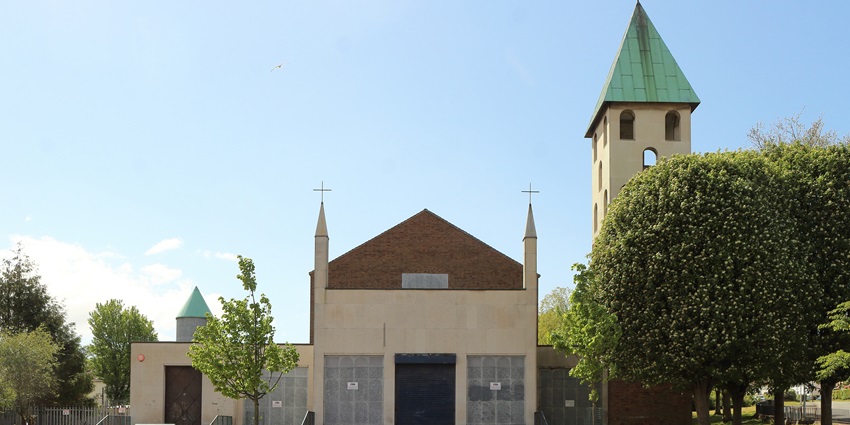 Front view of a closed church with a green-roofed bell tower and trees in foreground.