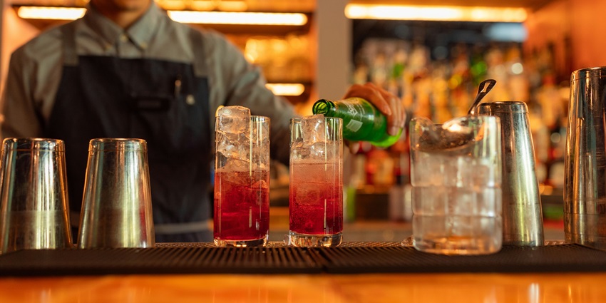 Image of a man making cocktails with pink drink clear glasses, ice cubes inside