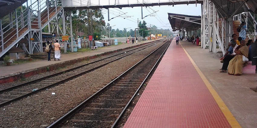 Image of a railway station and tracks in front, passengers sitting on the station waiting for the train