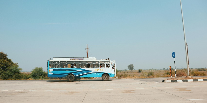 An old bus full of passengers on an empty road heading to the Rakhigarhi Museum.