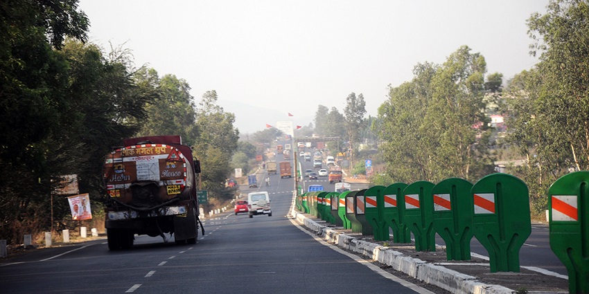 A view of Mumbai-Nashik Highway near a toll booth, with vehicles on the road and greenery in the background.