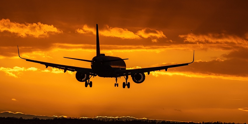 An aeroplane taking off during sunset with hue of orange skies.
