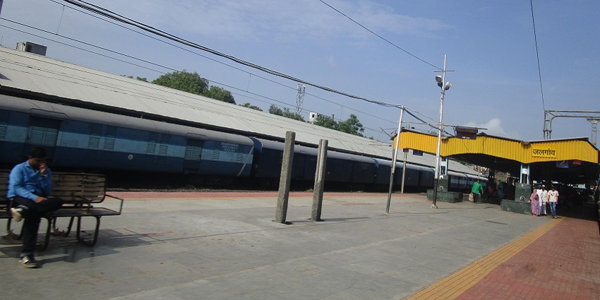 A blue train on the Jalgaon Junction railway platform with travellers passing by