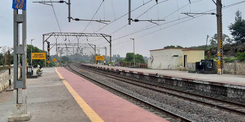Empty train tracks of Kamshet Railway station with a few passengers waiting near poles