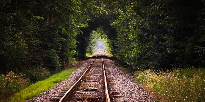 Railroad tracks stretching into the distance, surrounded by greenery and open landscape.