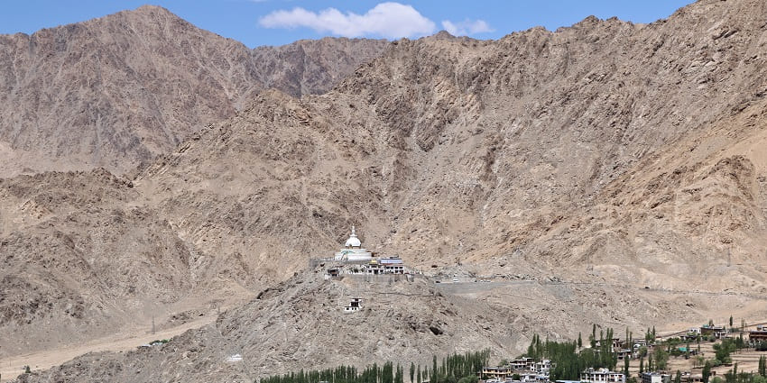 A picture of a monastery taken from a distance with mountains visible in the background