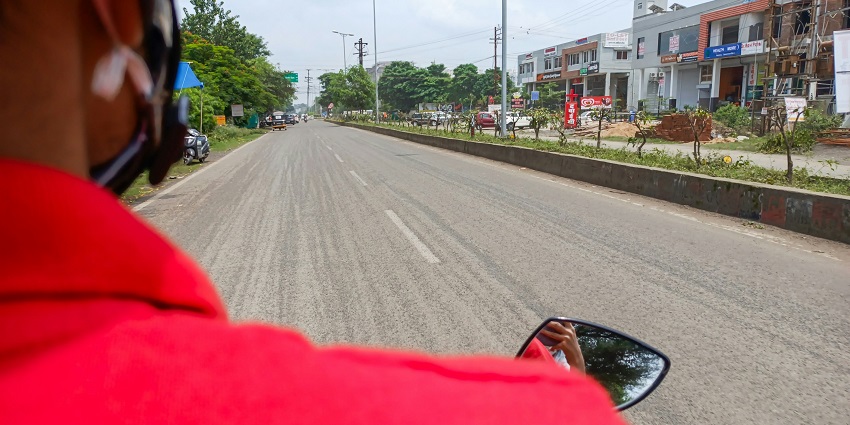 A person riding a bike on a road with shops and houses on either side, in India.