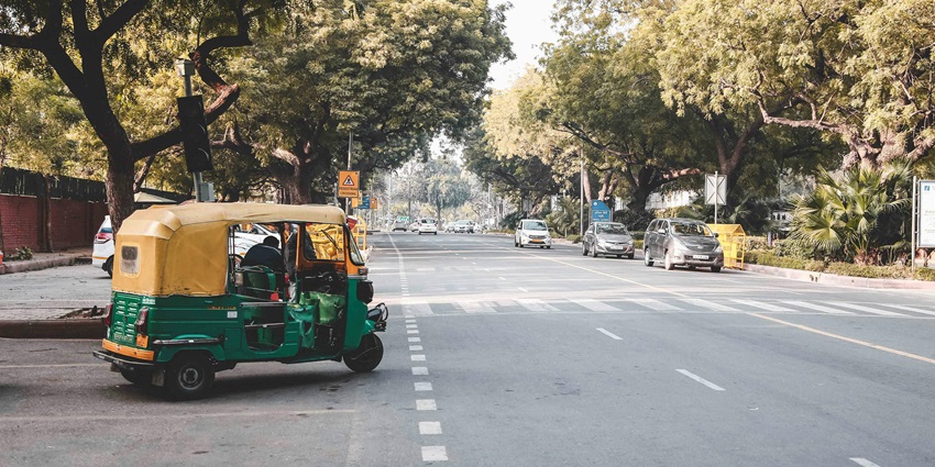 Traditional tuk-tuk driving on asphalt road near the Lotus Temple in Delhi.