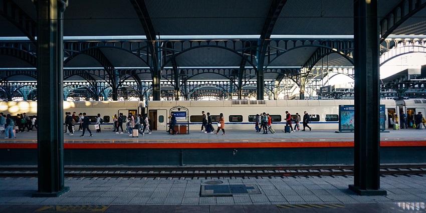 Busy railway train platform with passengers waiting and trains arriving and departing.
