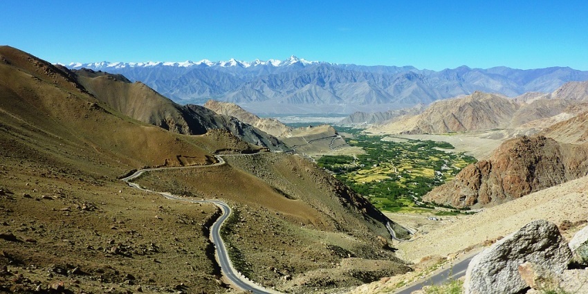 A scenic road in Leh, leading to Gogra Hot Springs surrounded by high mountains.