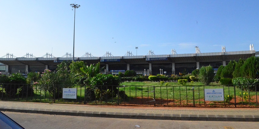 An image of the Madurai Airport terminal with a modern glass facade and lush greenery.