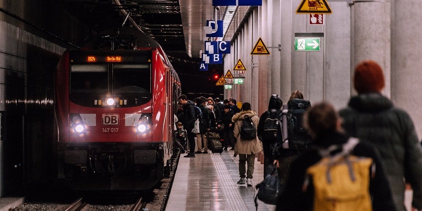 Train arriving at a bustling railroad station with travellers and vibrant surroundings.