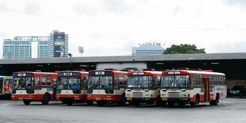 A frontal view of a bus stand with five buses parked in a line during the daytime.