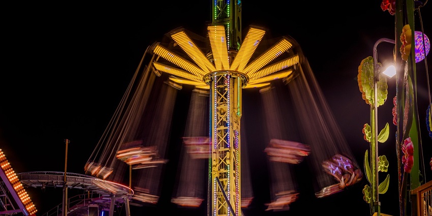 A vibrant theme park ride illuminated by colourful lights at night, with people enjoying.
