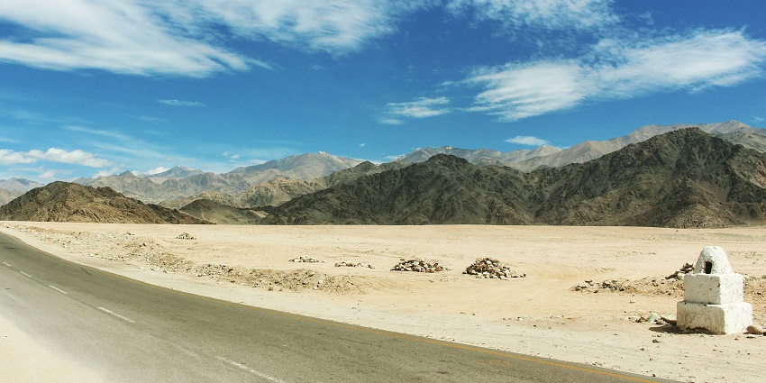 A stunning view of a grey road with rocky mountains in the background during the day.