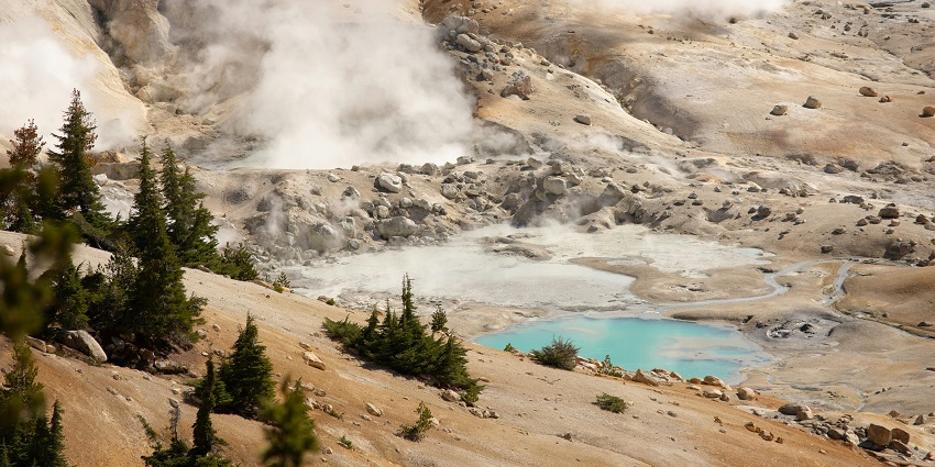Steaming hot spring amidst rugged terrains surrounded by pine trees