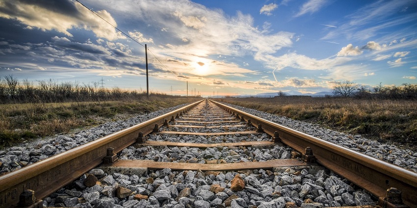 Railroad tracks stretching into the distance, surrounded by greenery and open landscape.