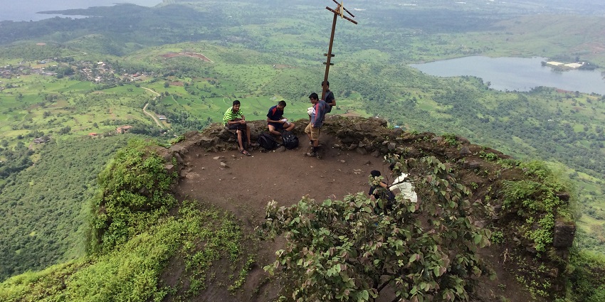 A wide view of Tikona Fort, with bright green trees and dramatic skies all around.