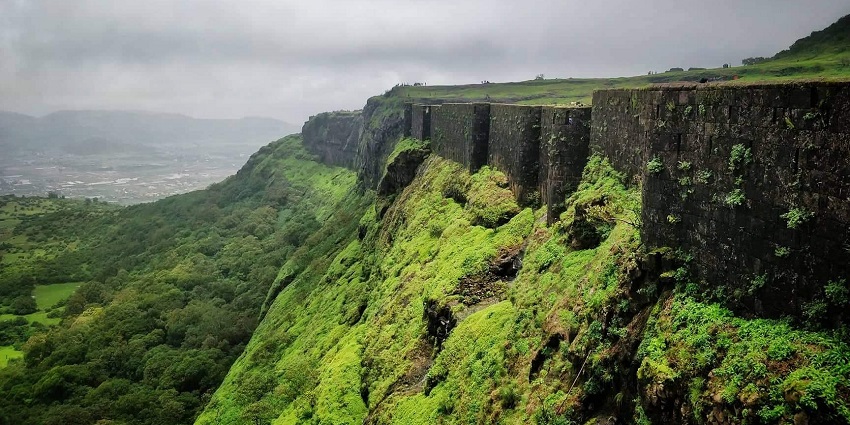The fortified stone wall of Visapur Fort in Pune, Maharashtra, with greenery in the background.