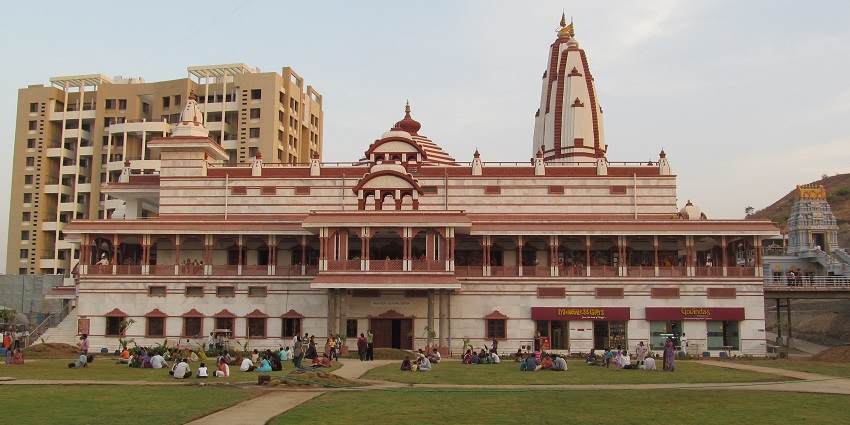 A picture of the ISKCON Temple in Pune taken from a distance with devotees sitting in the garden area