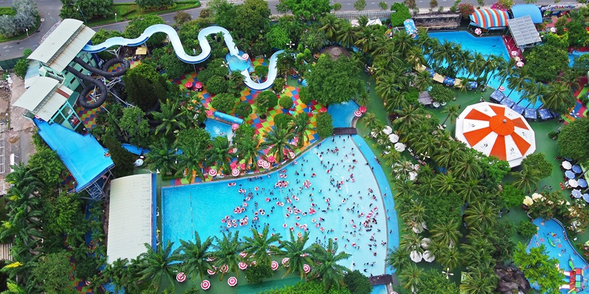 Number of people enjoying a water park full of slides and pools surrounded by trees