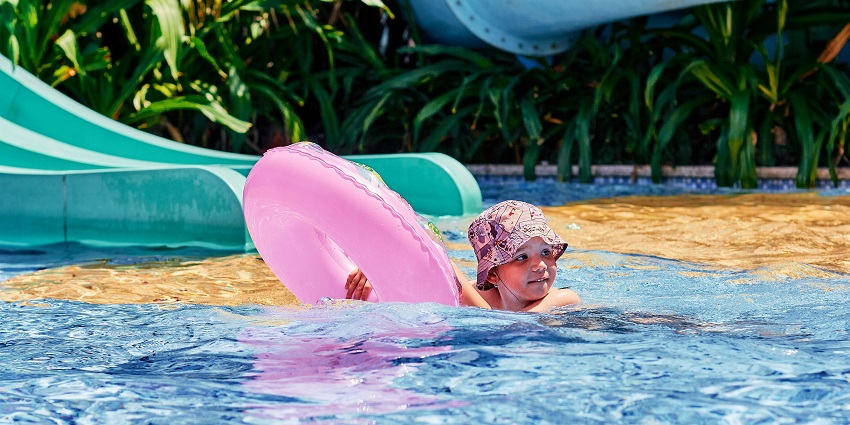A young boy swimming in a pool while holding onto an orange floater and having fun.