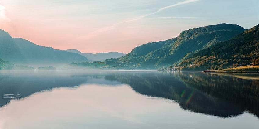 Honnamana Kere Lake reflects the sky, surrounded by green hills and trees.