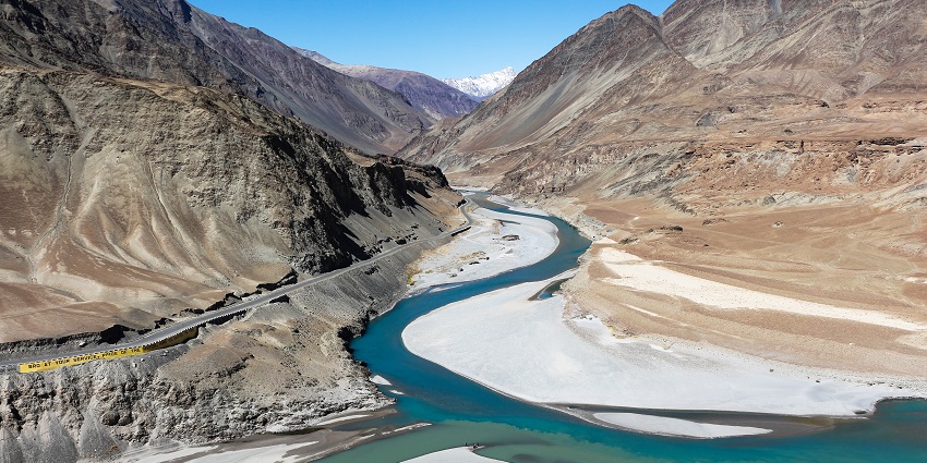 Image of confluence of Indus and Zanskar rivers, surrounded by mountains under blue sky