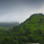 A view of Irshalgad Fort base in Maharashtra, featuring greenery and rugged terrain.