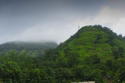 A view of Irshalgad Fort base in Maharashtra, featuring greenery and rugged terrain.