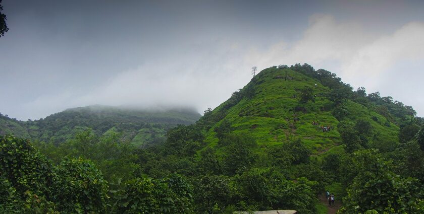 A view of Irshalgad Fort base in Maharashtra, featuring greenery and rugged terrain.