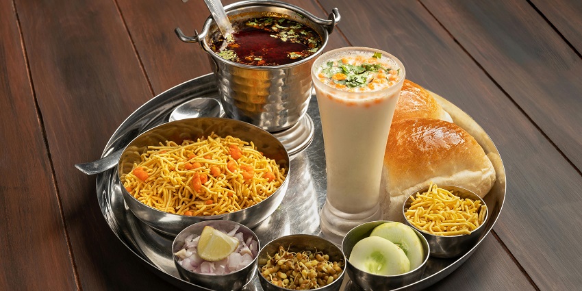 Kolhapuri Misal Pav served with a glass of buttermilk, red sauce, chopped onions and lemon