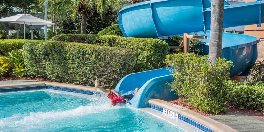An image of a boy sliding on through the water surrounded by green trees