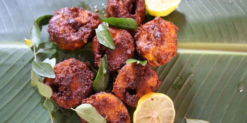 Numerous pieces of fried fish are served on a banana leaf with lemon wedges on the side.